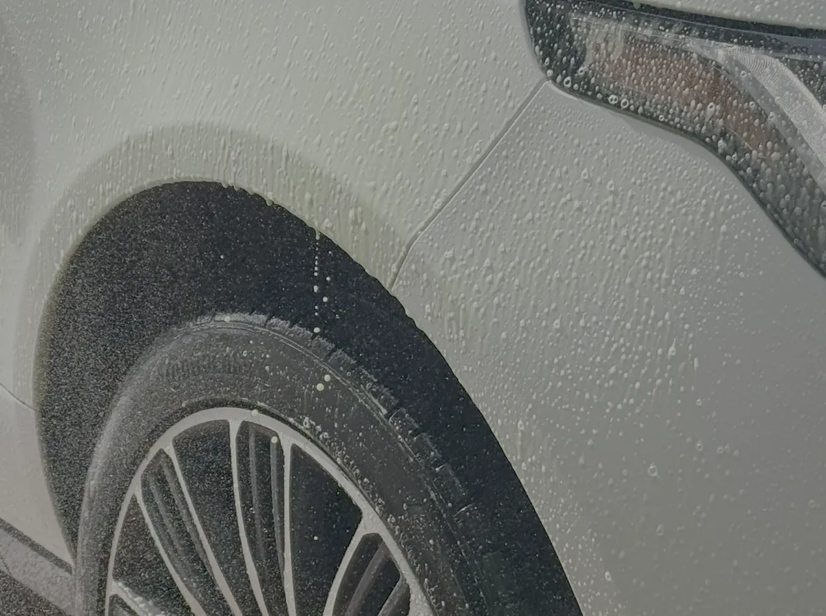 Suds sheeting off the wheel arch and alloy of a light-coloured SUV in a Glow self-serve bay.
